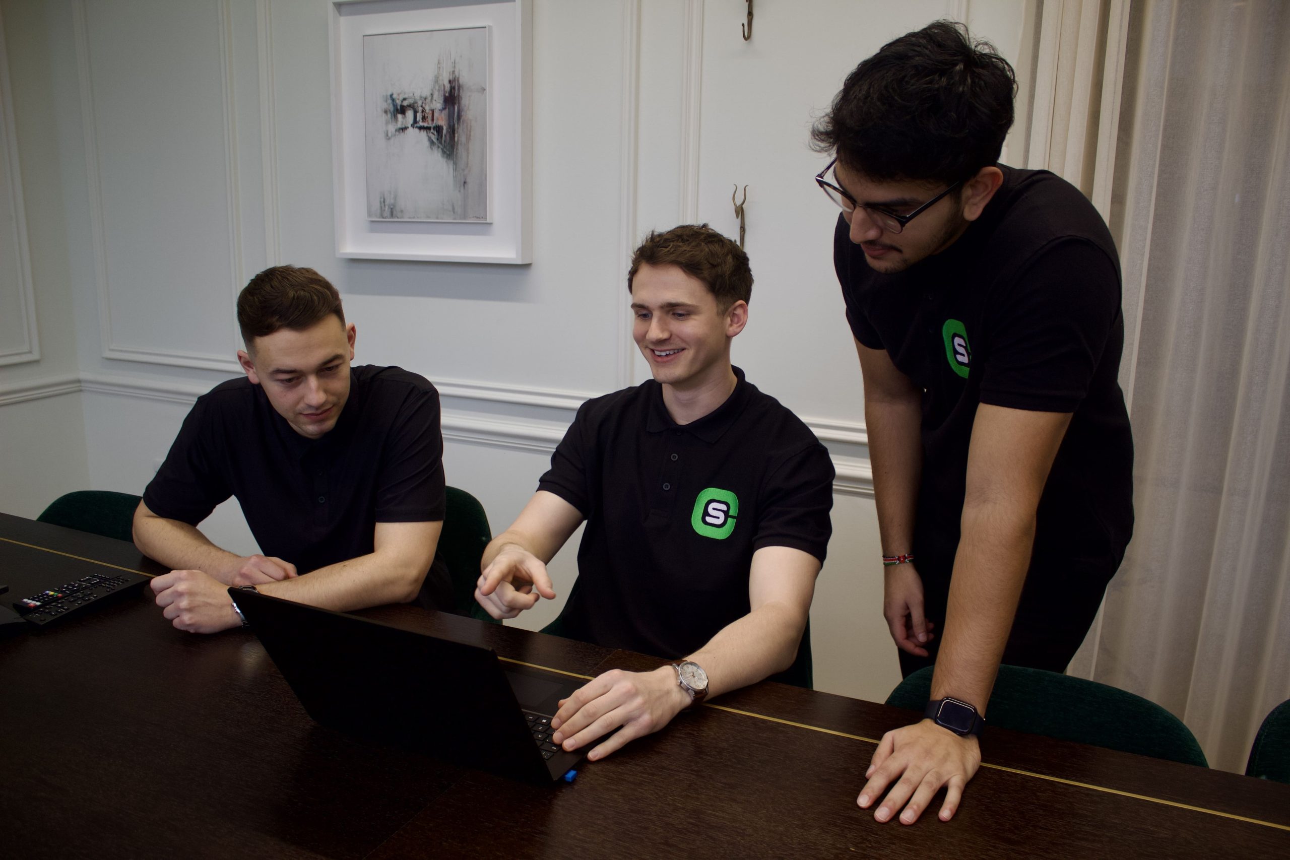 Three men laughing looking at a laptop in meeting room