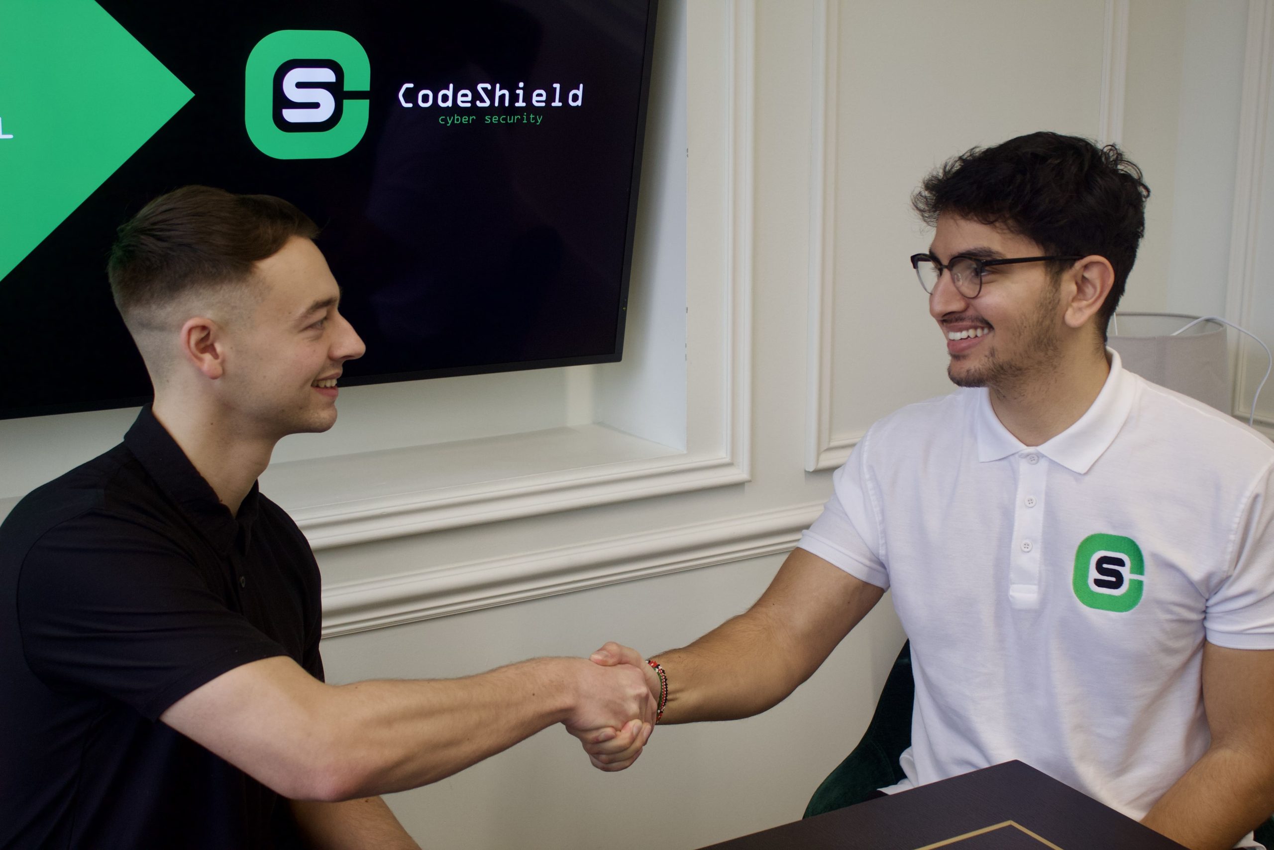 Two men shaking hands in front of TV